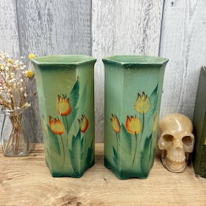Könnte beinhalten: Ein Paar sechseckige Keramikvasen mit einem grünen Farbverlauf und handgemalten orangefarbenen und gelben Tulpenmotiven mit grünen Blättern. Die Vasen haben eine weite Öffnung und einen zulaufenden Boden mit einer matten Oberfläche.