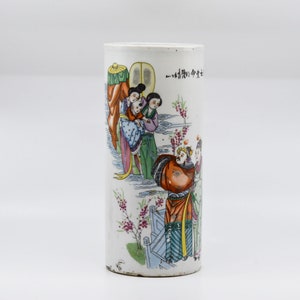 May include: A white porcelain cylinder vase with a colorful hand-painted scene of people in traditional Chinese clothing. The vase has a floral design and Chinese characters on the side.
