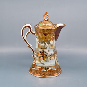 May include: A gold and white porcelain teapot with a detailed floral and landscape design. The teapot has a lid with a knob in the shape of a flower.