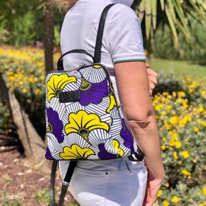 May include: A white and black backpack with a purple and yellow floral pattern. The backpack has a black zipper and a black strap.