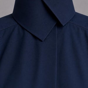 May include: A dark navy blue shirt featuring a high, structured stand-up collar with a pointed, overlapping front closure. The garment is crafted from a smooth, solid-colored fabric with clean, minimalist lines and visible shoulder seam stitching.