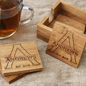 A set of four bamboo coasters with a matching caddie, custom engraved with a monogram and name. This personalized gift set includes free custom design and is shown with a glass tea mug on a white background. Perfect as a unique wedding, anniversary, or housewarming gift, featuring high-quality laser engraving on bamboo wood.