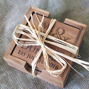 Puede incluir: Conjunto de cuatro posavasos de bambú en una caja de madera, atados con una cinta de rafia. Los posavasos están grabados con el texto "Mr. & Mrs. [Apellido] Est. Jul 16, 2016".