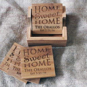 Puede incluir: Conjunto de seis posavasos de bambú con un soporte. Los posavasos están grabados con el texto "Home Sweet Home" y "The Orallos Est 7/21/16".