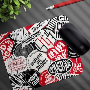 May include: A rectangular mousepad with a collage of black, white, and red sticker designs. The mousepad features various text elements, including "Welcome to the hot Megaverse" and "Walking on Water."