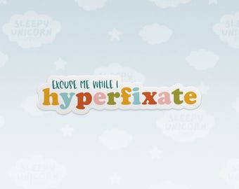 May include: A die-cut sticker featuring the text "EXCUSE ME WHILE I" in dark teal capital letters above the word "hyperfixate" in lowercase, multicolored letters including yellow, light blue, orange, pink, and olive green.