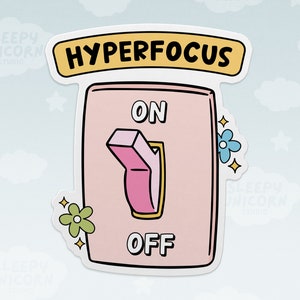 May include: A sticker featuring a pink light switch with the words "ON" and "OFF". The switch is in the "ON" position. Above the switch is a yellow banner that reads "HYPERFOCUS". Decorative flowers and stars surround the switch.