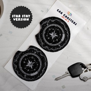 Könnte beinhalten: Ein Set aus zwei runden schwarzen Auto-Untersetzern mit weißem Sternenmotiv und dem Text STAR STAY VERSION. Die Untersetzer sind in einer weißen Hülle mit der Aufschrift CAR COASTERS SET OF 2 verpackt, dazu ein silberner Schlüsselanhänger in Autoform.