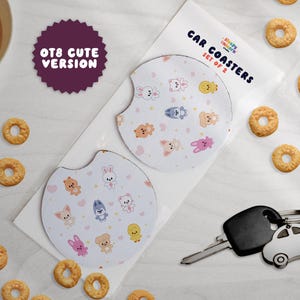 Könnte beinhalten: Ein Set aus zwei runden Auto-Untersetzern mit weißem Hintergrund und einem wiederkehrenden Muster aus kleinen, bunten Cartoon-Tierfiguren und rosa Herzen. Die Verpackung ist mit Car Coasters Set of 2 und OT8 Cute Version beschriftet.