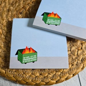 May include: Two light blue square sticky note pads featuring a graphic of a green dumpster on fire. The text on the dumpster reads, "OH LOOK... IT'S THE CONSEQUENCES OF MY OWN ACTIONS." The pads have a light gray bottom border.