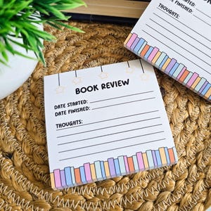 May include: A white book review notepad with a colorful striped border. The notepad has lines for writing the date started, date finished, and thoughts about the book. The notepad has a whimsical design with stars and hanging lights.