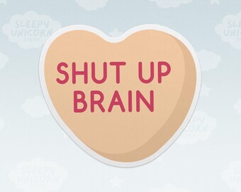 May include: A heart-shaped sticker with a light tan background and a white border. The text SHUT UP BRAIN is printed in the center in a bold, dark pink sans-serif font. The design has a smooth, matte appearance with a subtle shadow effect.