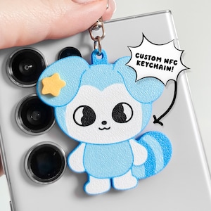 May include: A light blue and white 3D-printed character keychain with a yellow star on its ear and a striped tail. A white speech bubble graphic with a black outline points to the keychain, containing the black text CUSTOM NFC KEYCHAIN!