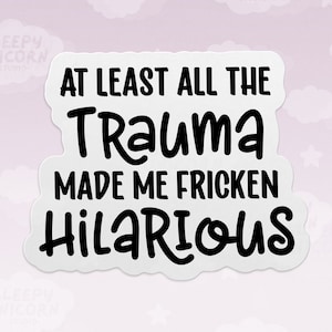 May include: A white sticker with the text "AT LEAST ALL THE Trauma MADE ME FRICKEN HILARIOUS" in black, bold, handwritten-style font. The sticker has a rounded edge and is set against a light pink background with white cloud graphics.