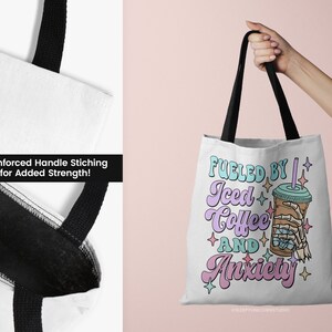 May include: White tote bag with black handles featuring the text "Fueled by Iced Coffee and Anxiety" in pastel colors. The design includes an iced coffee cup with a skeleton hand. Reinforced handle stitching is visible.