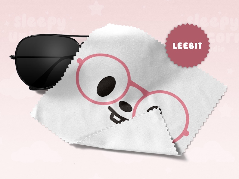 May include: Black aviator sunglasses rest on a white cleaning cloth with a pink glasses graphic. A maroon circular sticker with the text "LEEBIT" is in the upper right corner. The background is a soft pink.