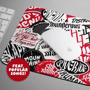May include: A rectangular mousepad with a collage of red, black, and white sticker-like designs and text. A white computer mouse rests on the pad, next to a white keyboard. The mousepad features the text "FEAT. POPULAR SONGS!"