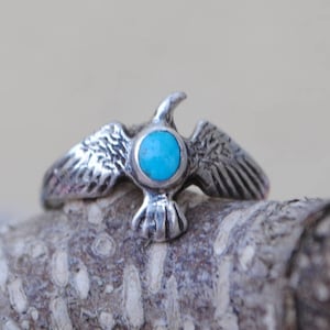 May include: A silver ring featuring a turquoise stone set in the centre, shaped like a bird with outstretched wings.