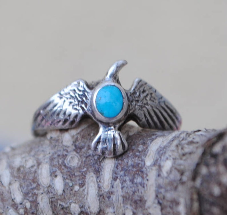 May include: A silver ring featuring a turquoise stone set in the centre, shaped like a bird with outstretched wings.