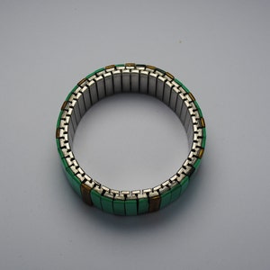 May include: A green and gold expandable bracelet made of metal links. The bracelet is made of small, rectangular pieces of metal that are connected together to form a flexible band.