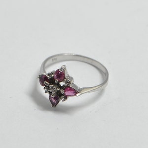 May include: A silver ring with a cluster of pink gemstones and smaller clear stones set in a flower shape.