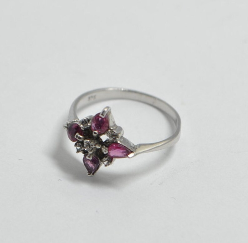 May include: A silver ring with a cluster of pink gemstones and smaller clear stones set in a flower shape.