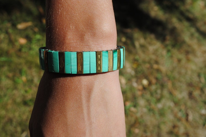 May include: A turquoise and gold bracelet with geometric patterns. The bracelet is made of small, rectangular tiles.