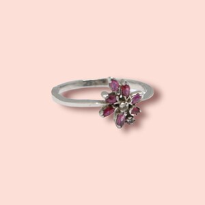 May include: A silver ring with a pink flower design. The flower is made of small pink stones.