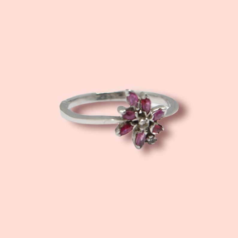 May include: A silver ring with a pink flower design. The flower is made of small pink stones.