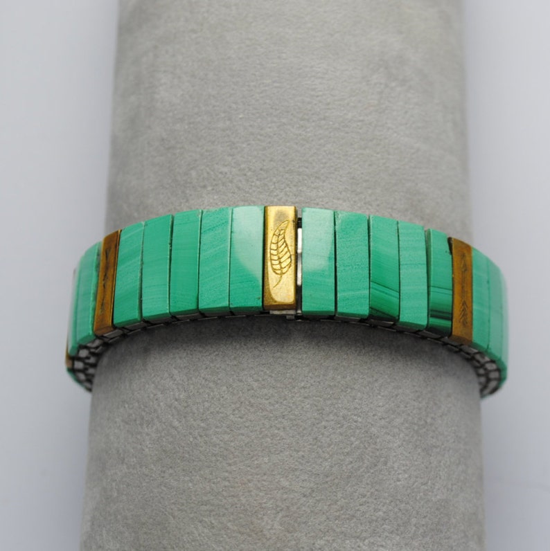 May include: A green and gold bracelet with a leaf design. The bracelet is made of small, rectangular tiles.