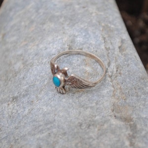 May include: A silver ring featuring a turquoise stone and an eagle design.