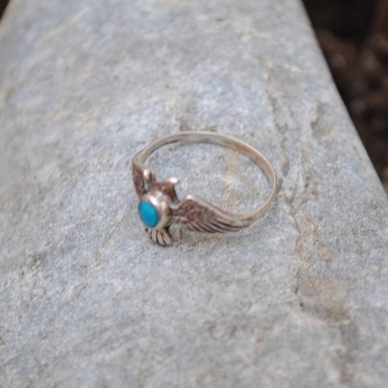 May include: A silver ring featuring a turquoise stone and an eagle design.