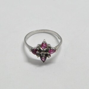 May include: A silver ring with a cluster of pink and white gemstones set in a starburst design.