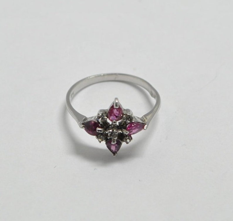 May include: A silver ring with a cluster of pink and white gemstones set in a starburst design.