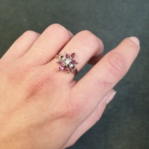 Op de afbeelding: Een zilveren ring met een bloemmotief met roze en witte edelstenen.