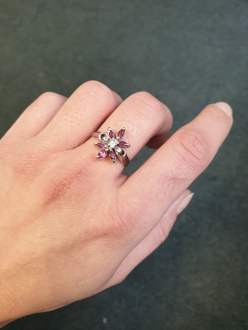 Op de afbeelding: Een zilveren ring met een bloemmotief met roze en witte edelstenen.