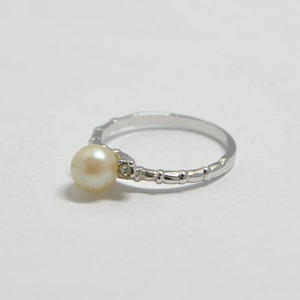 May include: A silver ring with a single pearl and a small clear stone accent.