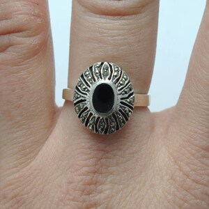 May include: A silver ring with a black oval stone surrounded by marcasite stones.