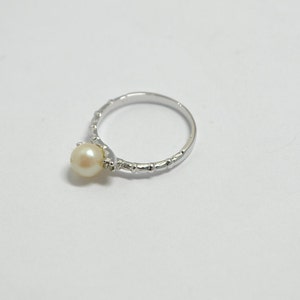 May include: A silver ring with a single white pearl set in the center. The band of the ring is textured with small bumps.