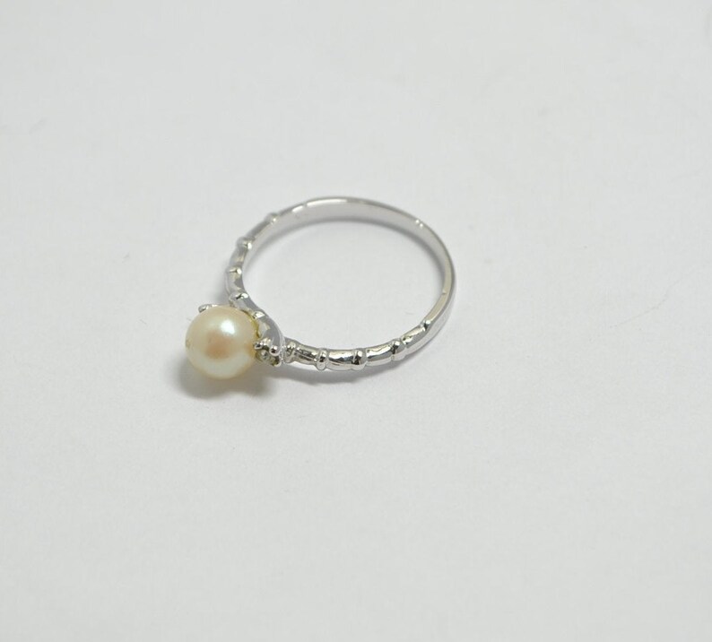 May include: A silver ring with a single white pearl set in the center. The band of the ring is textured with small bumps.