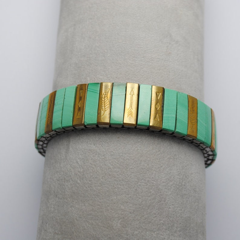 May include: A green and gold bracelet with a stretchy band. The bracelet is made of small, rectangular tiles with different symbols and designs, including arrows, leaves, and geometric shapes.
