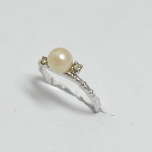 May include: A silver ring with a white pearl and two small clear stones.