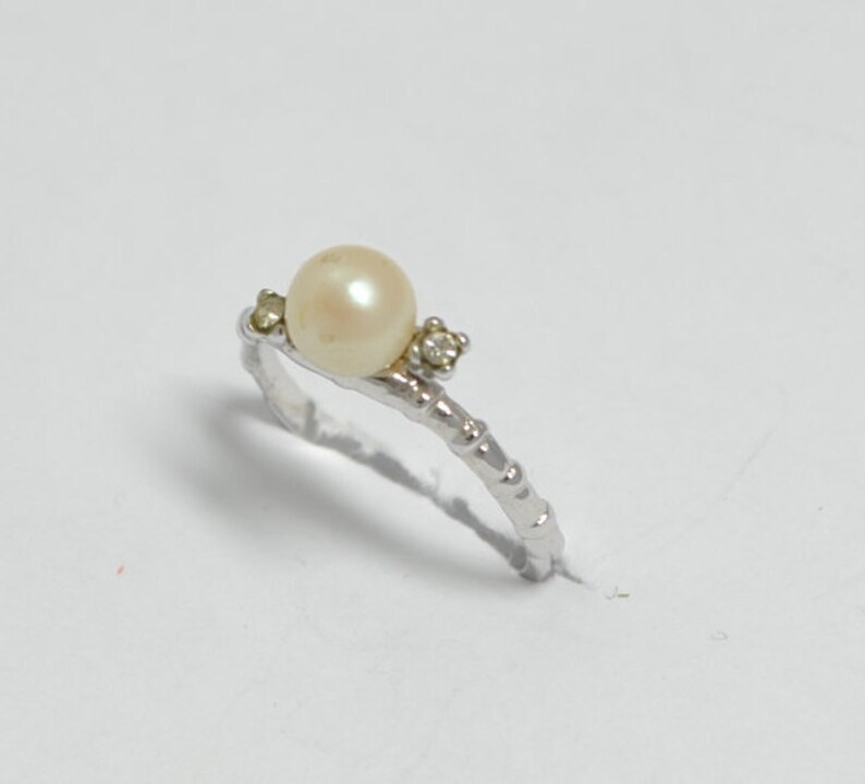 May include: A silver ring with a white pearl and two small clear stones.