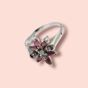 Op de afbeelding: Een zilveren ring met een bloemmotief bezet met roze en witte edelstenen.
