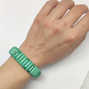 May include: A green malachite bracelet with a stacked design. The bracelet is worn on a person's wrist.