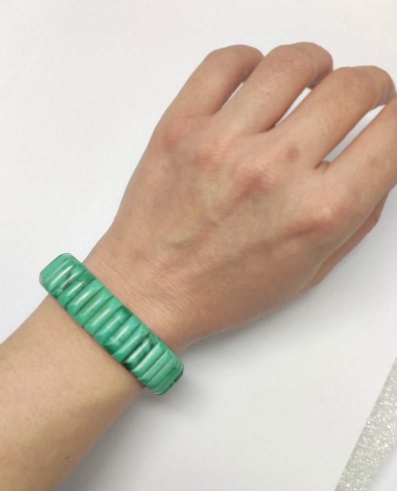 May include: A green malachite bracelet with a stacked design. The bracelet is worn on a person's wrist.