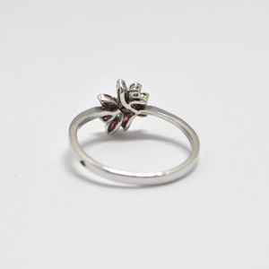May include: A silver ring with a floral design featuring pink gemstones. The ring is set on a white background.