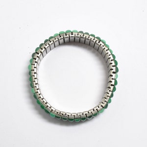 May include: A silver expandable bracelet with green gemstone accents.