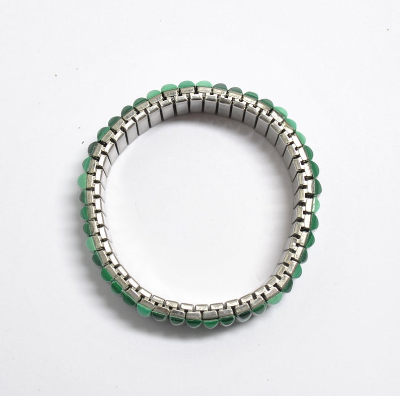 May include: A silver expandable bracelet with green gemstone accents.