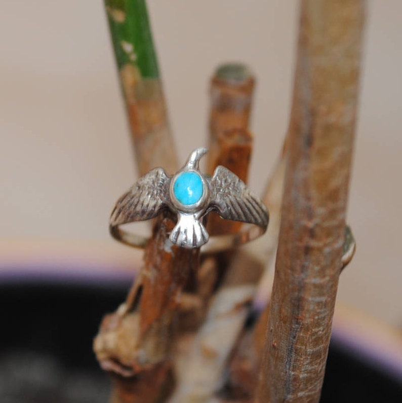 May include: A silver ring featuring a turquoise stone set in the centre, shaped like a bird with outstretched wings.